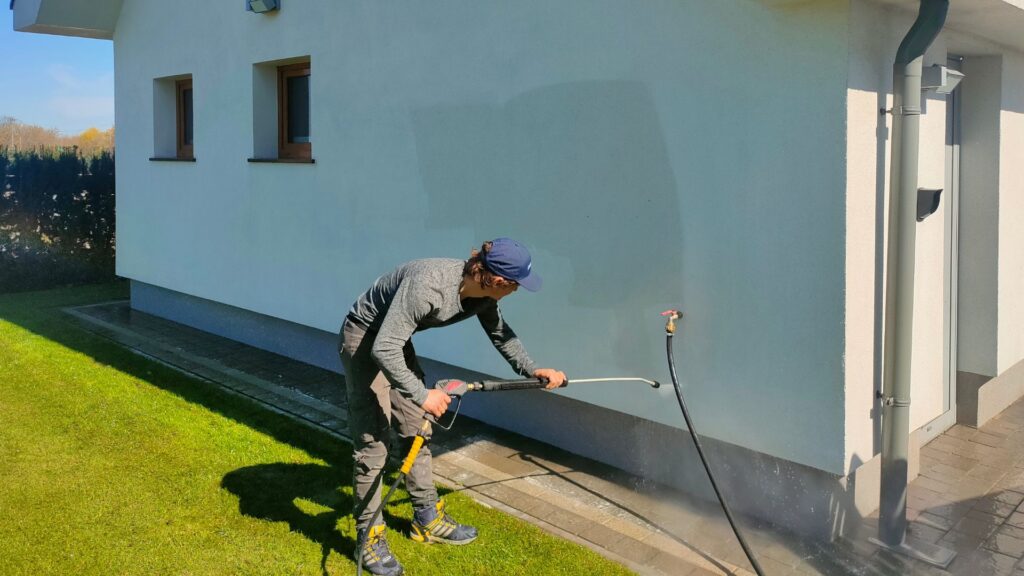 mężczyzna myje elewację budynku myjką ciśnieniową